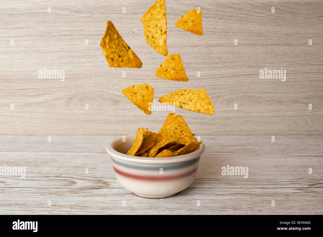 Nachos Späne fliegen und fallen in eine Schüssel auf einen hölzernen Tisch Stockfoto