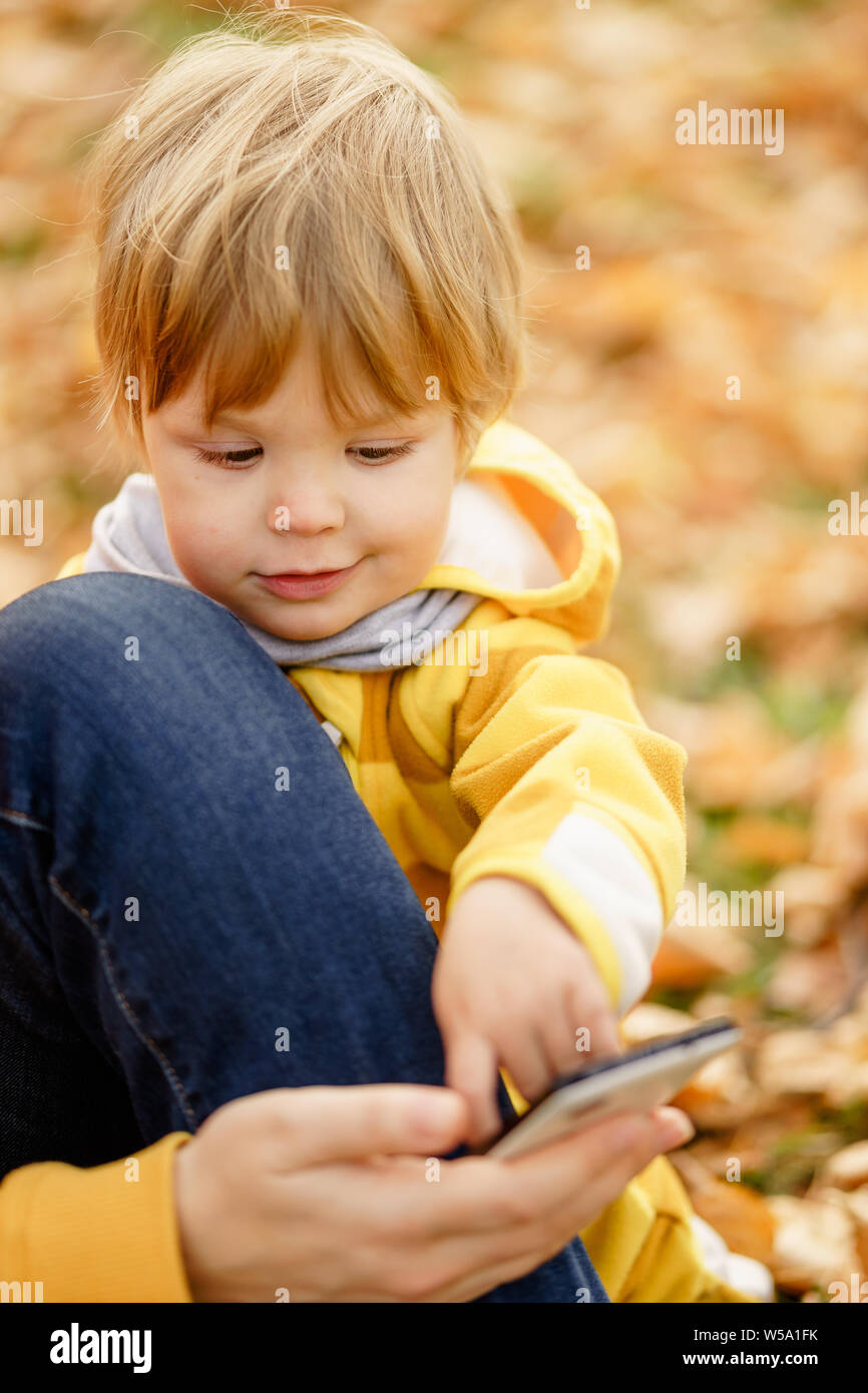 Konzept: Familie, Kinder. Glückliches Kind, baby boy Lachen und Spielen mit der Mutter Smartphone im Herbst auf der Wanderung in der Natur draußen im Park Stockfoto
