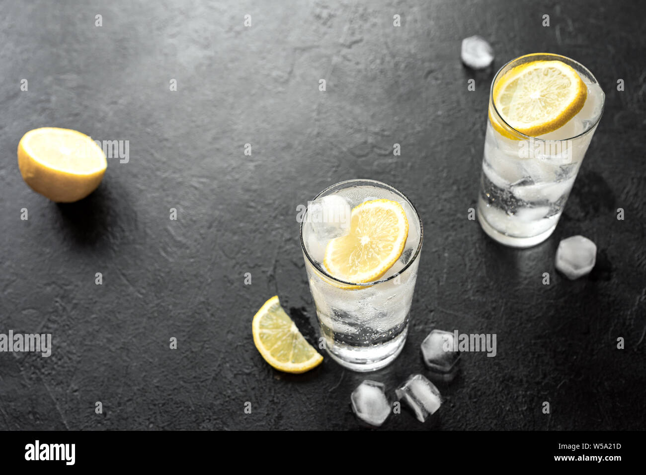 Alkohol trinken (Gin Tonic Cocktail, Wodka Cocktail, Tom Collins Cocktail) mit Zitrone und Eis auf rustikalen schwarzen Stein Tabelle, Kopieren, Ansicht von oben. So vereist Stockfoto