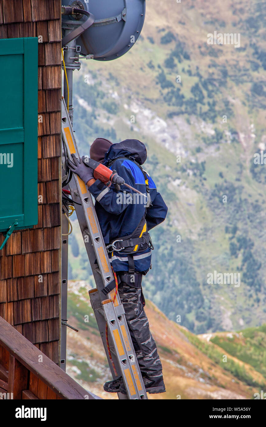 Mitarbeiter mit Tools stehen auf der Treppe auf ein hölzernes Haus in den Bergen Stockfoto