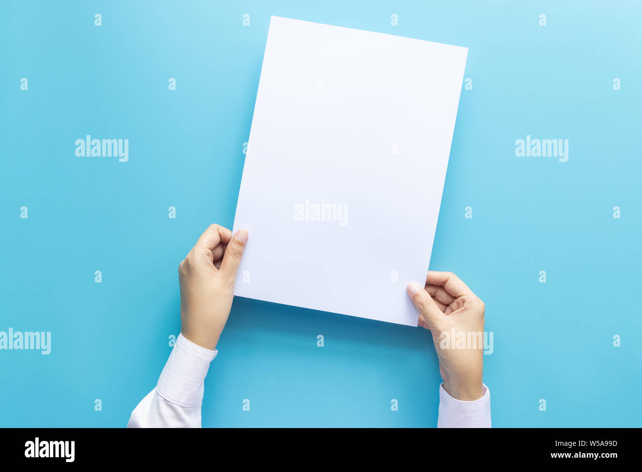 Die Hände schließen Holding leere weiße Leere schreiben Papierformat A4 für Flyer oder Einladung mock up auf einem blauen Hintergrund. Stockfoto
