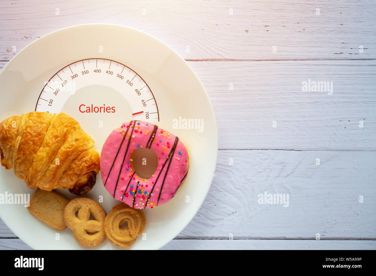 Kalorien zählen und die Lebensmittelüberwachung Konzept. Donut, Croissant und Cookies auf weiße Platte mit Zunge Skalen für Kalorien messen Stockfoto