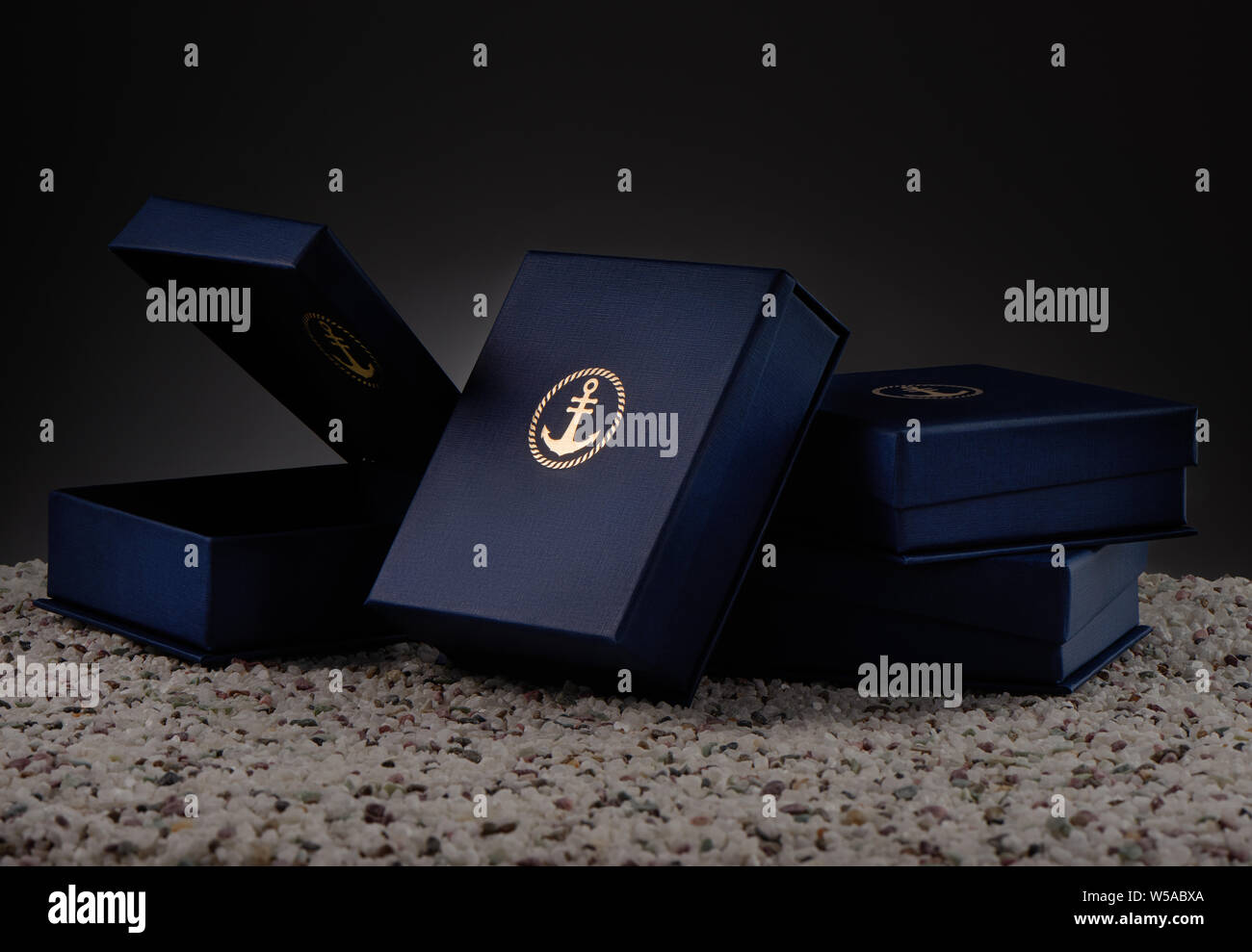 Blau Geschenkboxen mit Emblem des Goldenen Anker auf Meer Kiesel Stockfoto