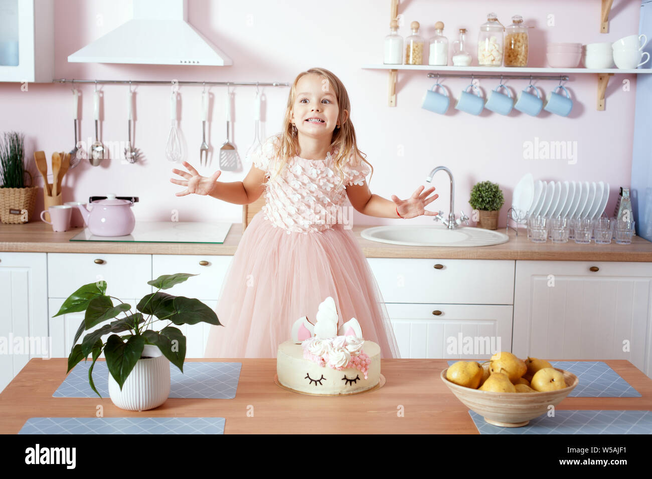 Kleines Mädchen in einem schönen Kleid in der Küche herum. Es ist wie ein Kuchen auf dem Tisch. Stockfoto