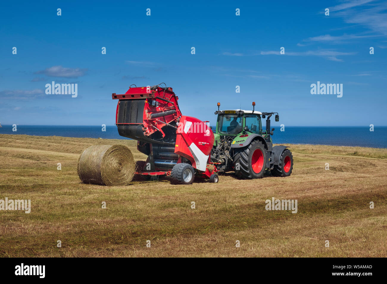 Moderne Landmaschinen - ein Bauer im Traktor, runde Heuballen mit einem Lely Welger RP 445 eine erweiterte variable Rundballenpresse. Stockfoto