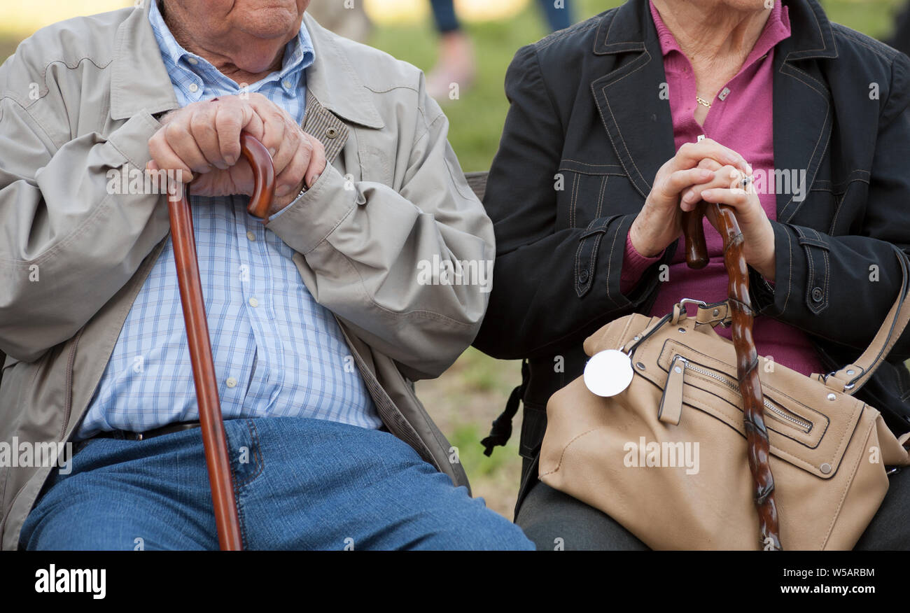 Senior Paar Hände halten, während auf der Parkbank sitzen zusammen. Pensionierter Mann und Frau mit Spazierstock. In der Nähe der Hände. Stockfoto