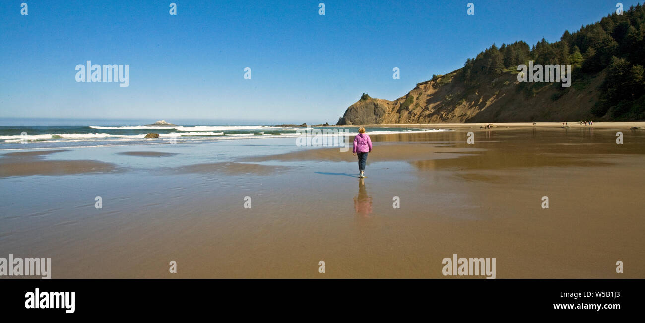 Eine Frau nimmt einen Strandspaziergang an einem weiten Sandstrand an der California Pacific Coast in der Nähe von Lincoln City, Oregon. Stockfoto
