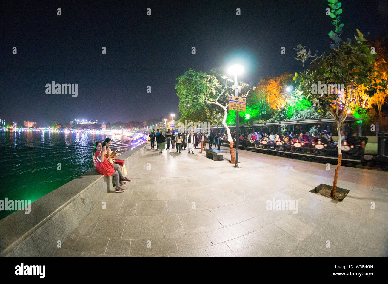 Ahmedabad, Gujarat, Indien - ca. 2018: Leute sitzen auf den kreisförmigen Bereich um kankaria See in Ahmedabad. Die schönen bunten Abend Leuchten ein Stockfoto