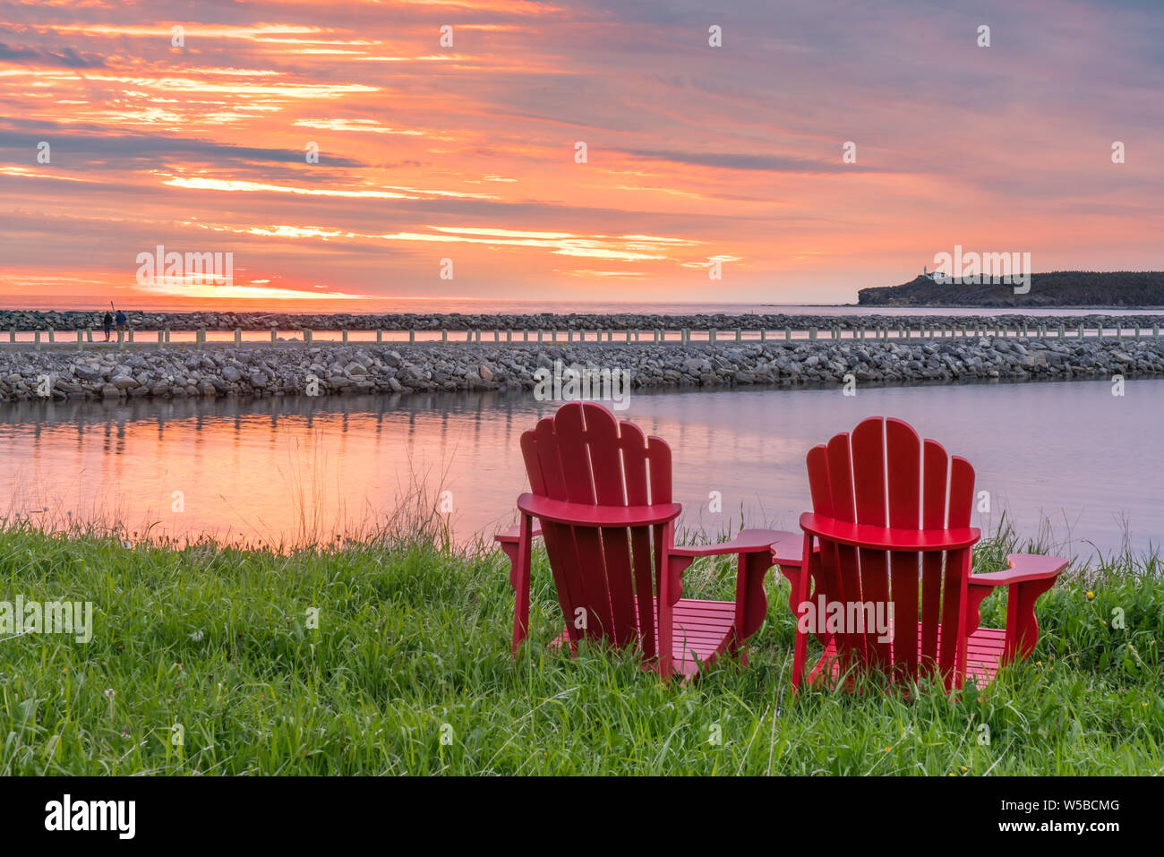 Red adirondack Stühle entlang dem Meer bei Sonnenuntergang in Rocky Harbour, Neufundland, Kanada Stockfoto