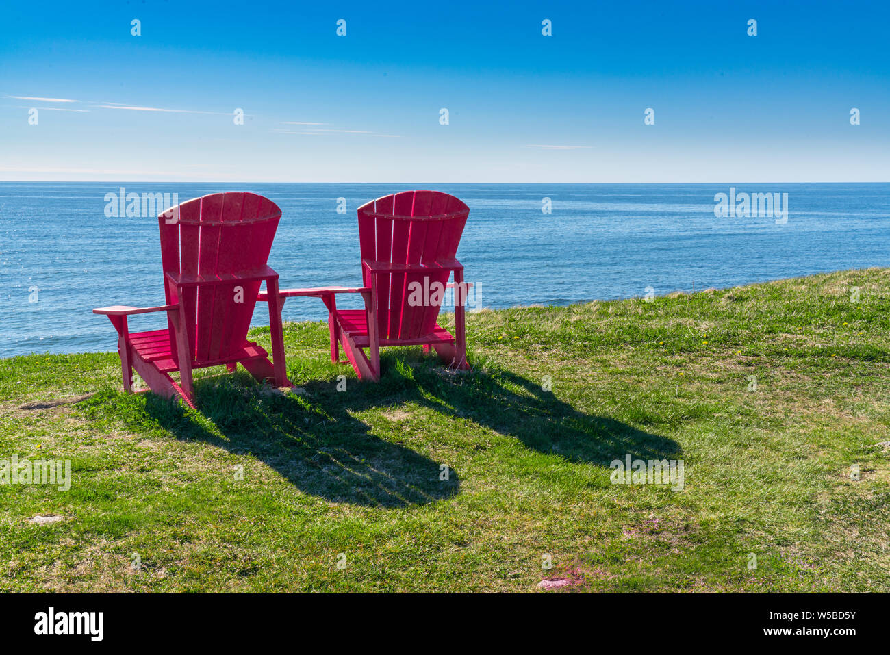 Zwei rote Adirondack Stühlen mit Blick auf den Ozean an der Küste von Neufundland im Gros Morne National Park, Kanada Stockfoto
