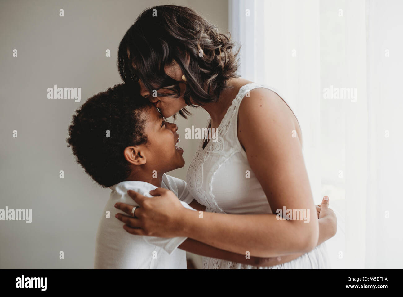 Die Mutter küsst zärtlich schulpflichtigen Sohn Stirn, während umfassende Stockfoto