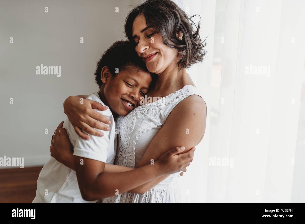 Mutter umarmt schulpflichtigen Sohn lächelnd im Studio umfassen Stockfoto
