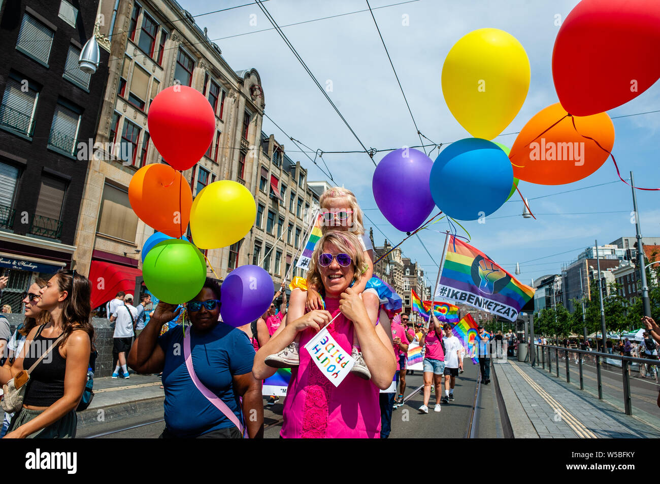 Eine Frau ihr Kind trägt mit Ballons während der Stolz. Weil der Stonewall 50. Jahrestag, der Stolz in diesem Jahr das Thema "Erinnern Sie sich an die Vergangenheit, die Zukunft gestalten'. Der Stolz ist eine demonstrative und Aktivist zu Fuß vom Homomonument zu den Vondel Park. Dies ist der 'Gegenstück' der Welt-berühmten Boot Parade, die stattfindet, eine Woche später, am 5. August. Tausende von Menschen durch die Flaggen der Länder, in denen Homosexualität im Strafgesetzbuch ist beteiligt. Stockfoto