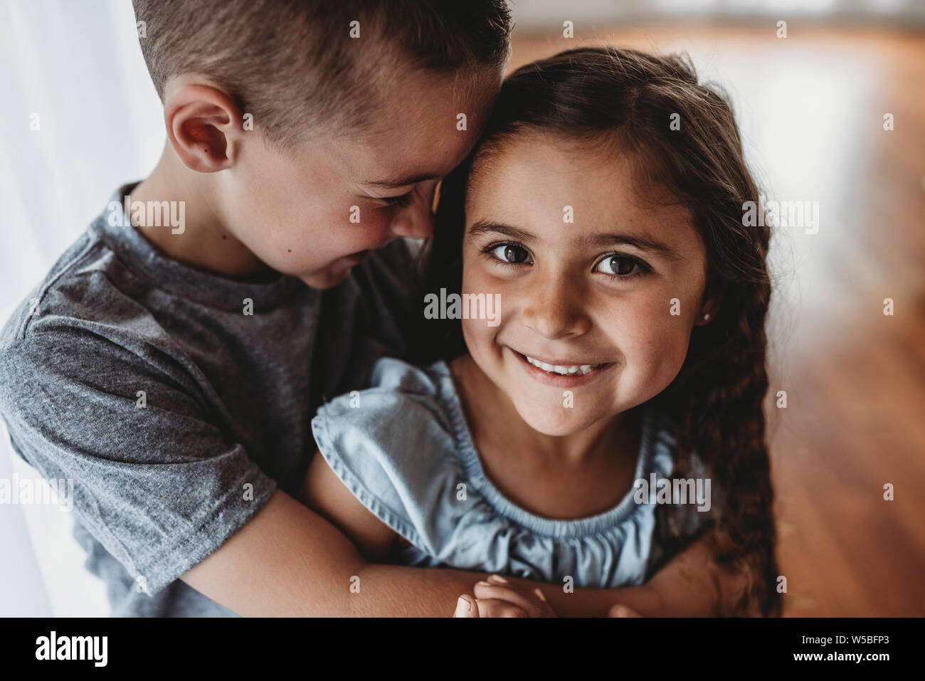 Porträt eines jungen Mädchens während Bruder umarmt sie und lacht Stockfoto