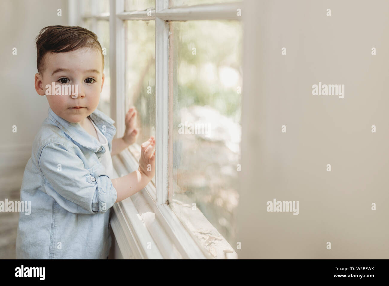 Toddler boy auf Kamera durch Fenster in natürlichem Licht studio Stockfoto
