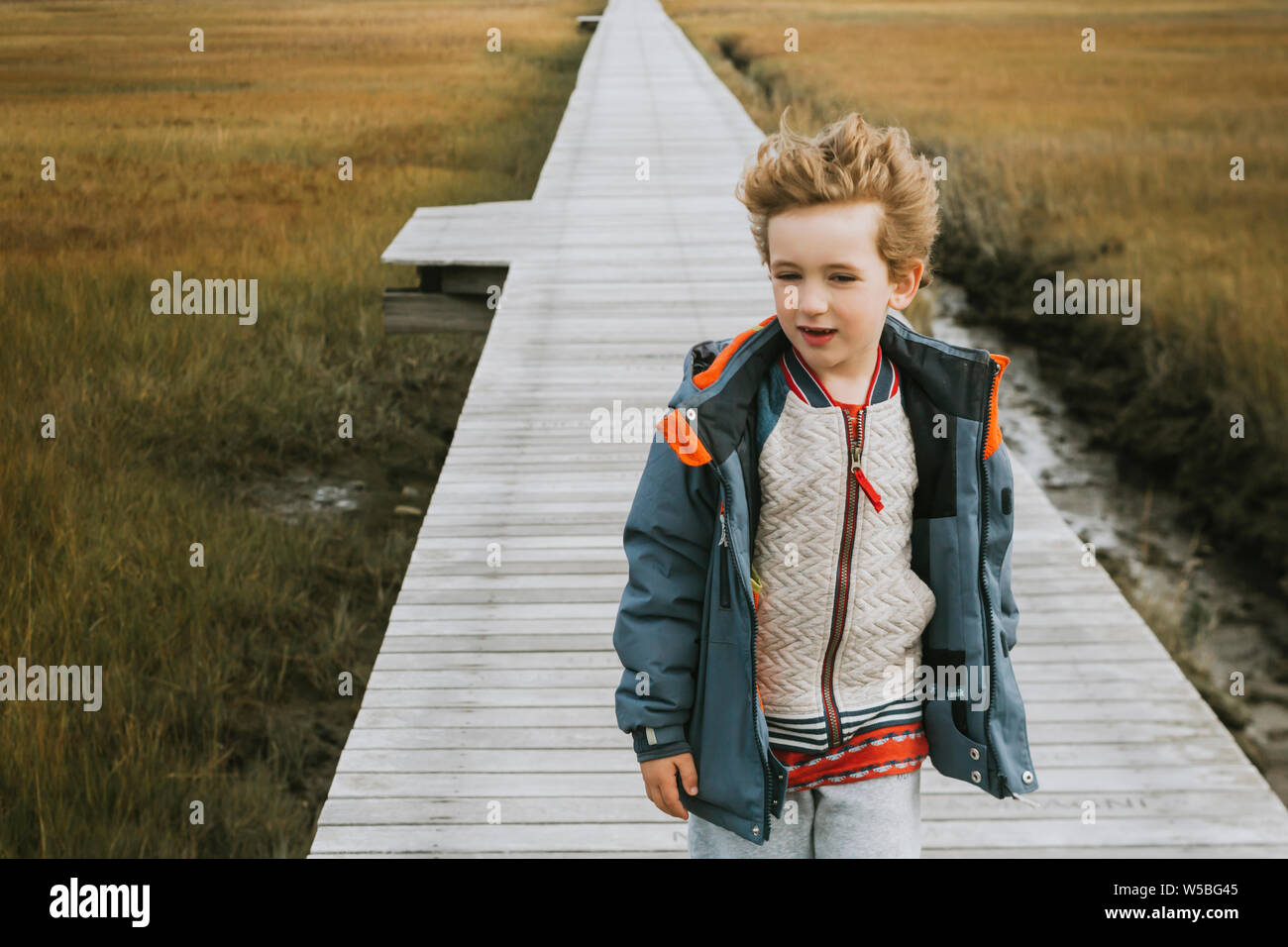 Cute windswept Junge zu Fuß entlang der Promenade über Salt Marsh Stockfoto