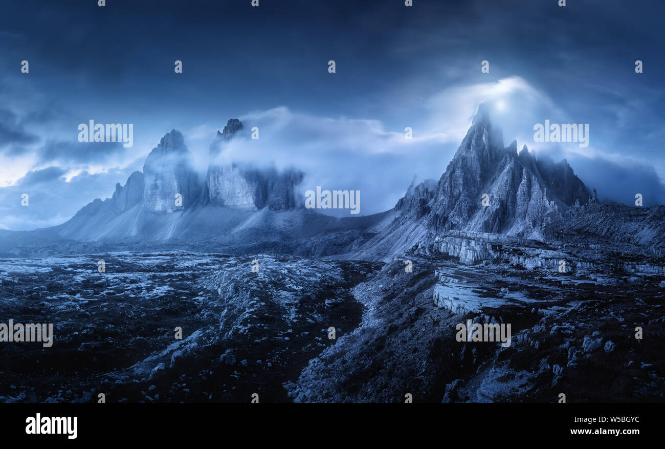 Berge in Nebel auf schöne Nacht. Verträumte Landschaft mit Bergspitzen, Steine, Gras, blauer Himmel mit unscharfen niedrigen Wolken, Sterne und Mond. Felsen an d Stockfoto