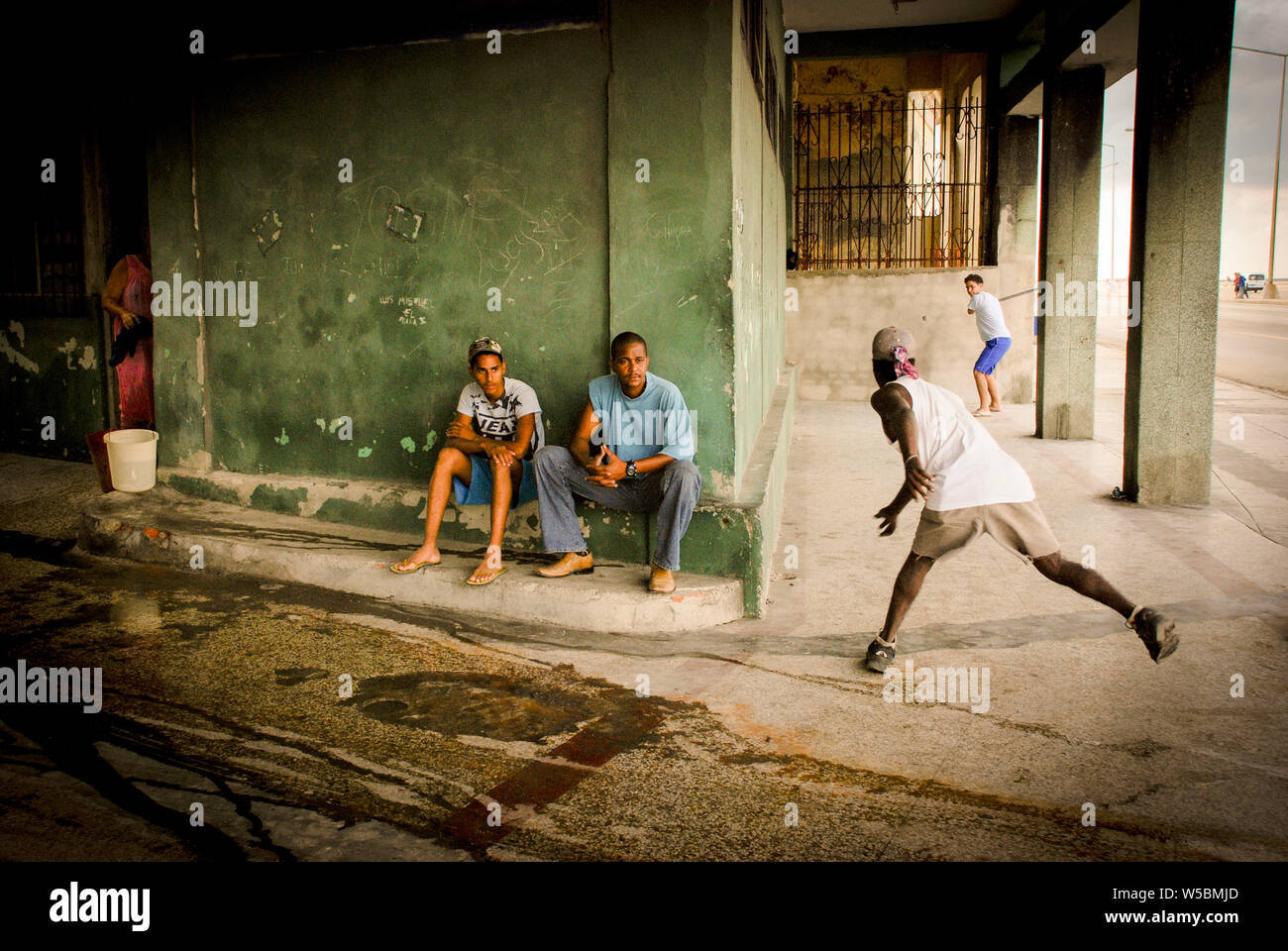 Kinder Baseball spielen auf einem Bürgersteig in Havanna, Kuba als Dame Mops und reinigt Ihr Haus Stockfoto