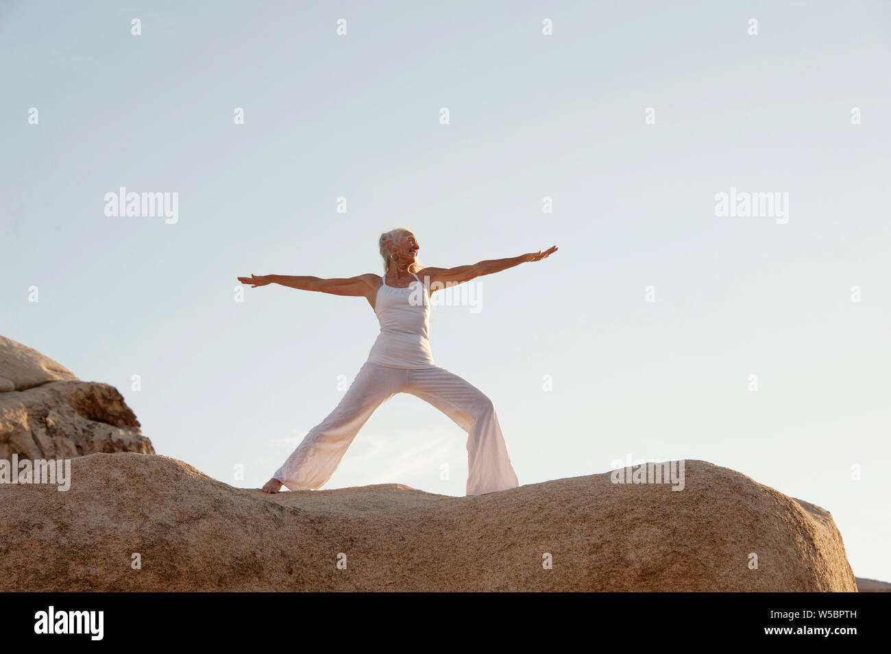 Reife Frau in Krieger 2 yoga Pose auf dem Felsen. Stockfoto