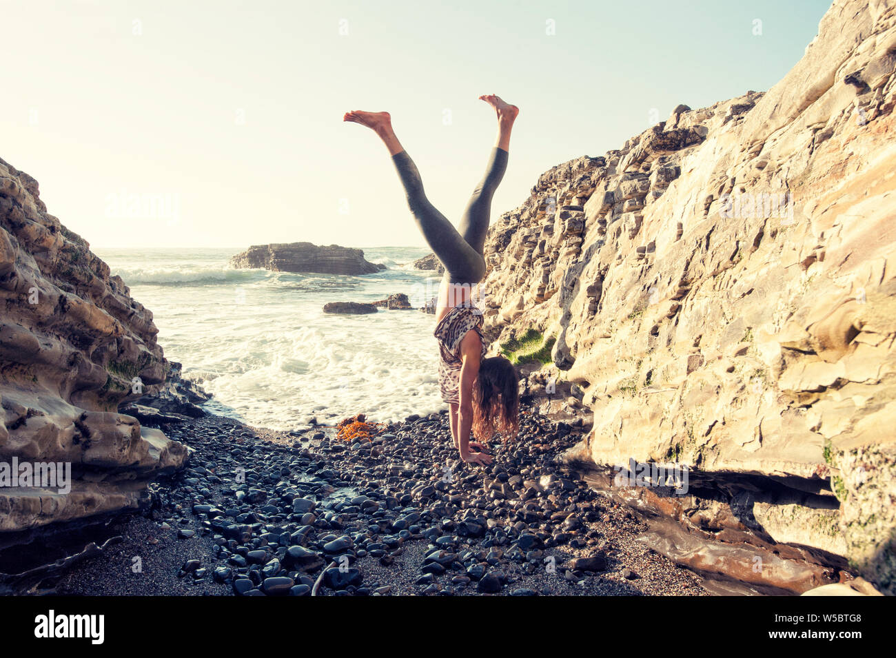 Energie und Vitalität ausdrücken, die durch eine junge passende Frau auf einem wilden und felsigen Strand. Stockfoto