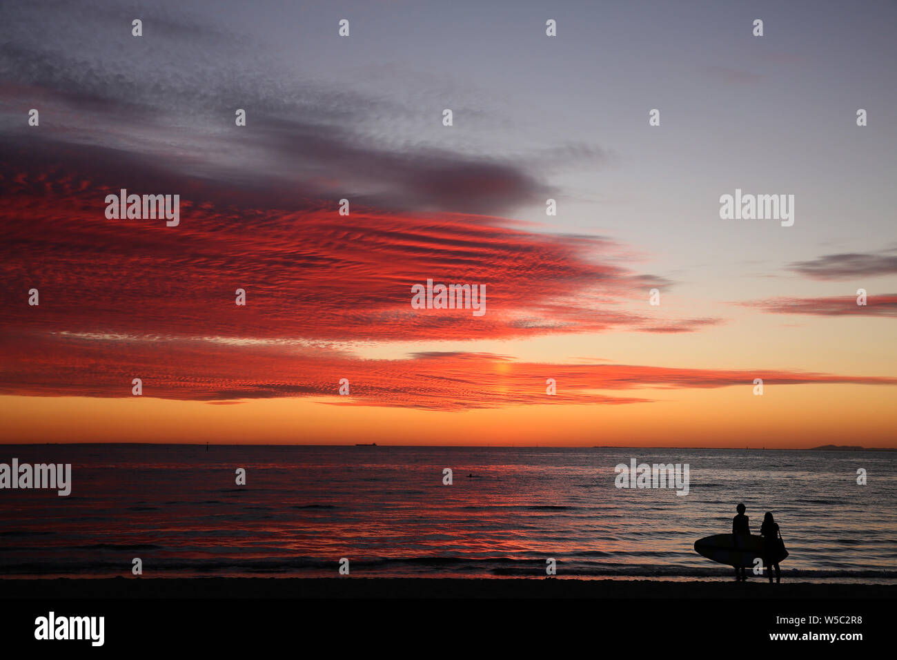 Leuchtend rote Melbourne Sonnenuntergang mit Stand Up Paddleboarder und seine Freundin in Sillhouette in St. Kilda Beach, Port Philip Bay, Victoria, Australien Stockfoto