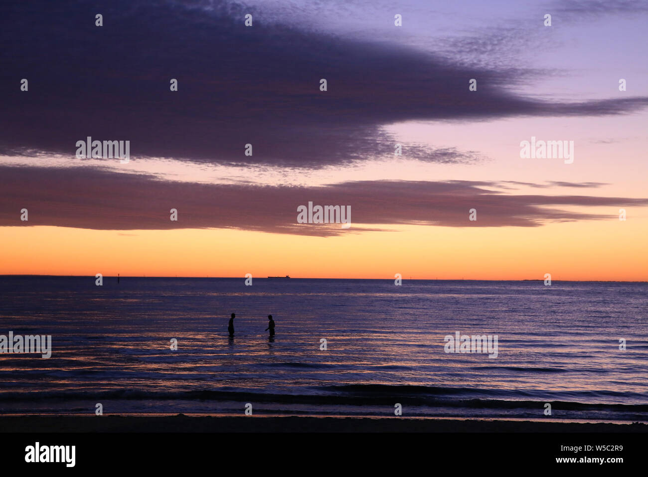 Lila und Orange Melbourne Sonnenuntergang mit Schwimmer bei St Kilda Strand Port Philip Bay. Victoria, Australien Stockfoto