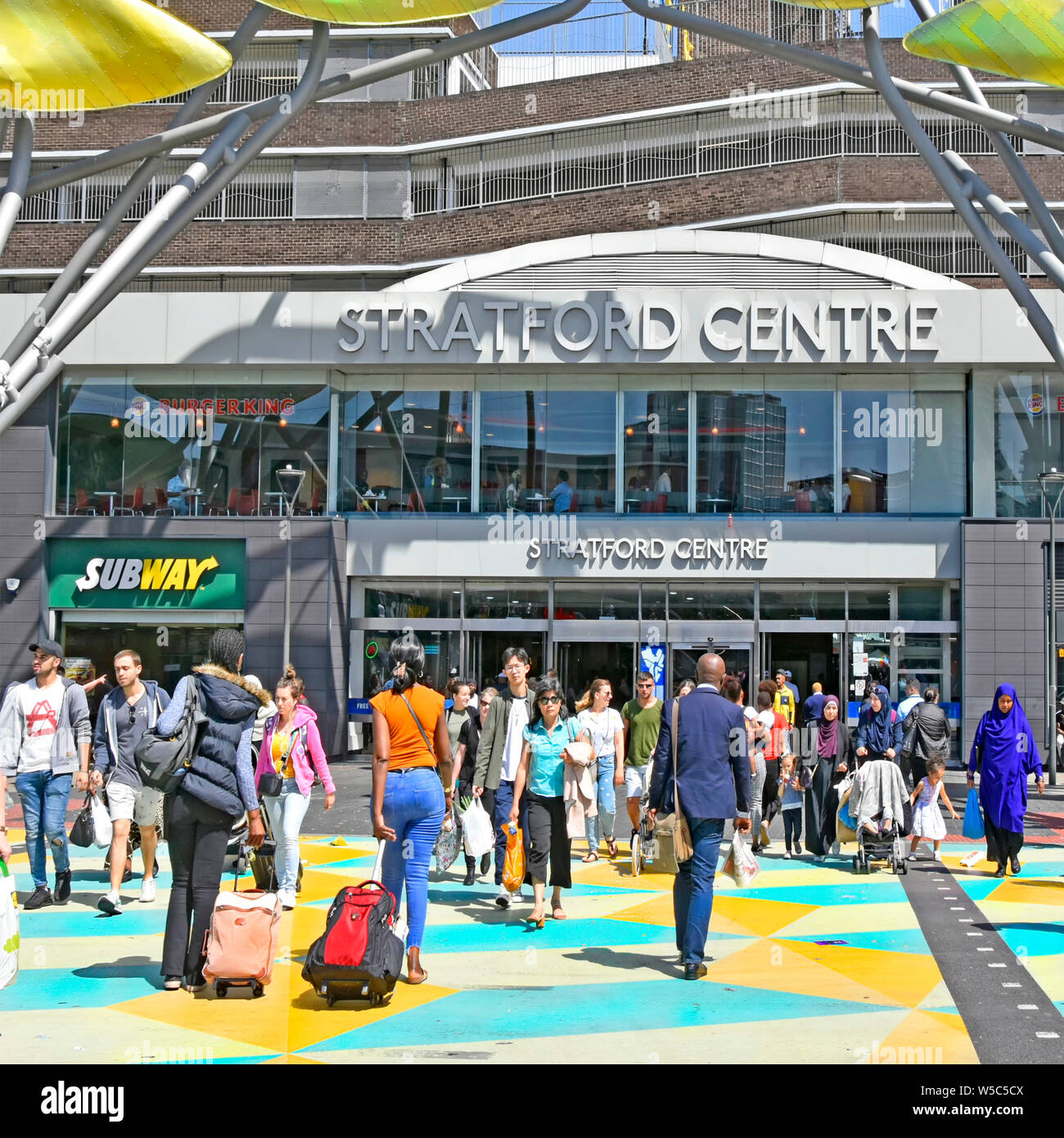 Vielfältige Gruppe von Menschen auf der belebten Fußgängerzone überqueren der Straße in hellen Farben links Stratford Einkaufszentrum & Bahnhöfe & Westfield Geschäfte East London Großbritannien Stockfoto
