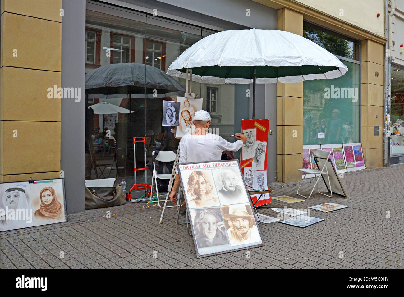 Heidelberg, Deutschland - Juli 2019: Street Artists sittin unter dem großen Sonnenschirm und Portraits von Menschen auf der Straße von Heidelberg Stockfoto