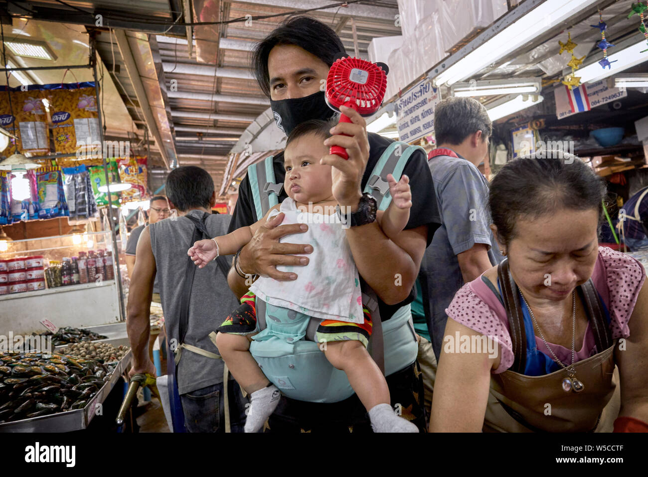 Heiße Wetter Leute kühlen ab. Vater trägt Kind und mit einem Handventilator, um sich in der Hitze eines Thailand Indoor-Markt kühl zu halten. Stockfoto