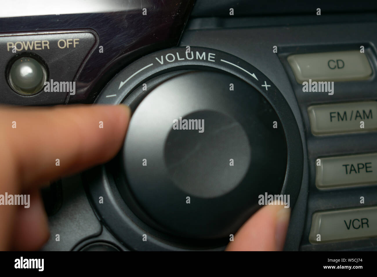 Eine Person dreht den Lautstärkeregler nach oben oder unten (der Fokus liegt dabei auf dem Wort 'Volumen' auf das Gerät geschrieben) Stockfoto