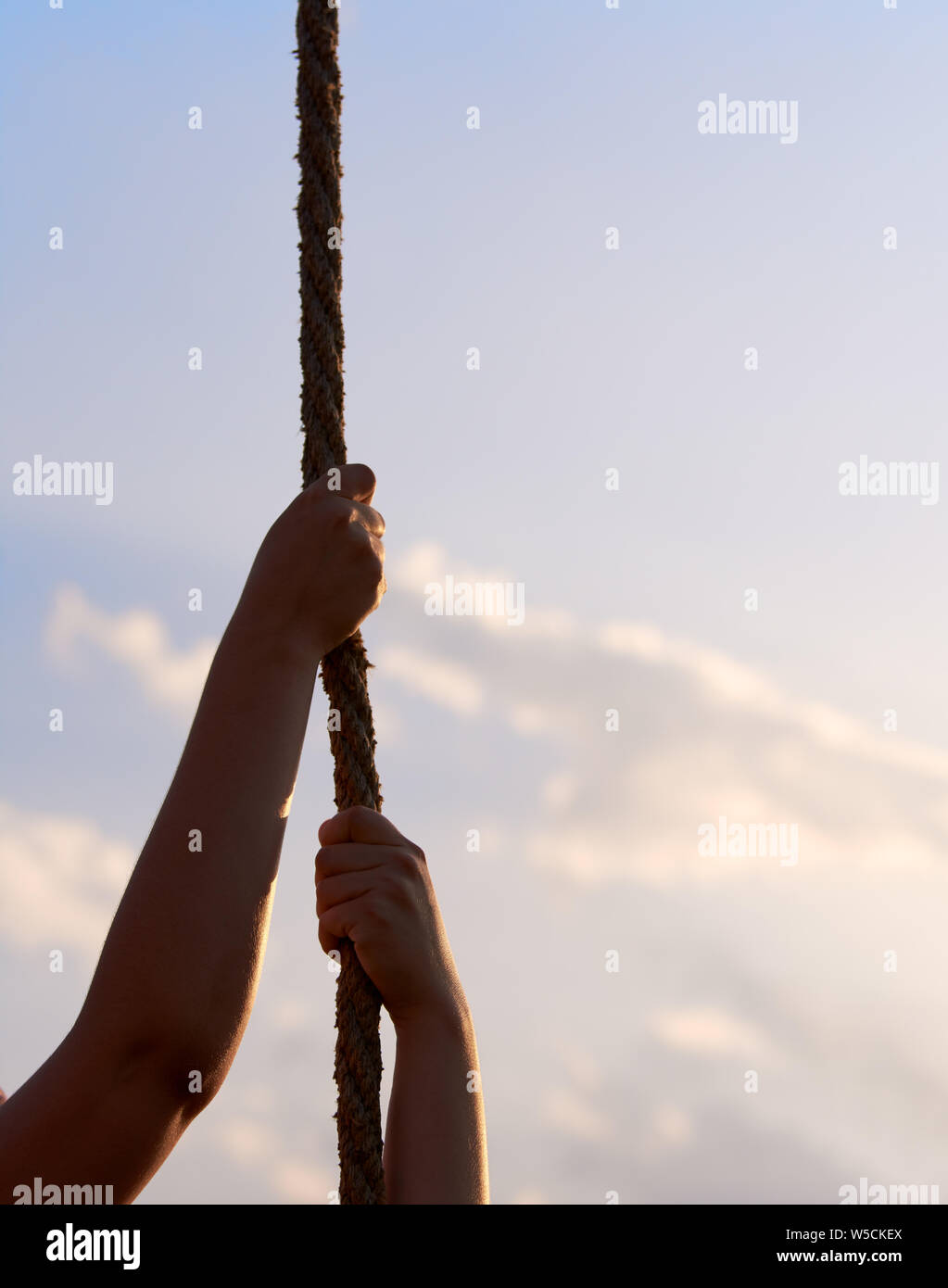 Junge Frau oder ein Mädchen hält die Hände an Seil und steigt im Sportunterricht der Klasse. Blauer Himmel mit Wolken. Stockfoto
