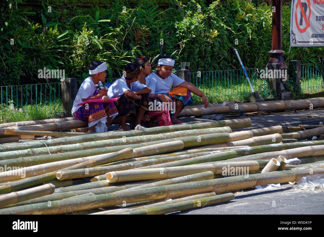 Vier Jungen im Schatten sitzen neben Stapeln von Bambus Gerüst während der Bauarbeiten in Ubud, Bali, Indonesien Stockfoto