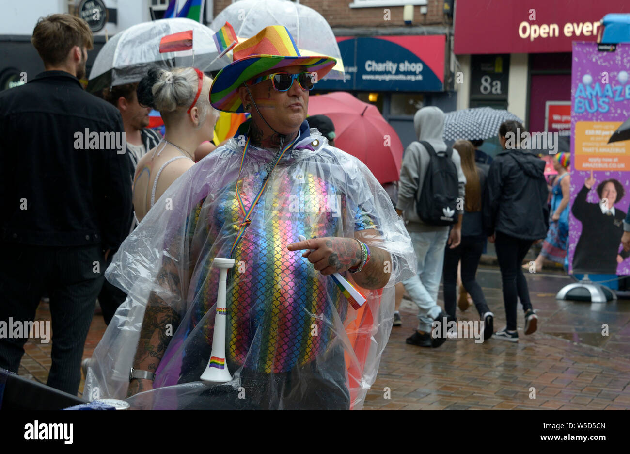 Alte Kerl in Regenbogen, Hut & Shirt, mit klaren Regencape, im Pride event Stockfoto