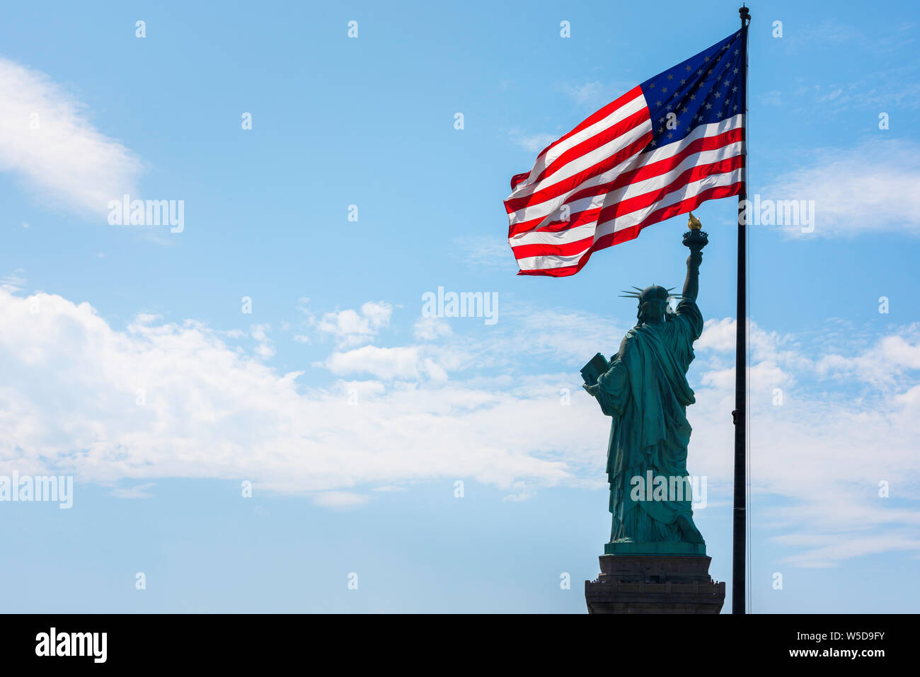 Freedom Concept Bild, Blick auf die Rückseite der Freiheitsstatue und eine hinterleuchtete Stern- und Streifenfahne mit Kopierraum links, New York City, USA. Stockfoto