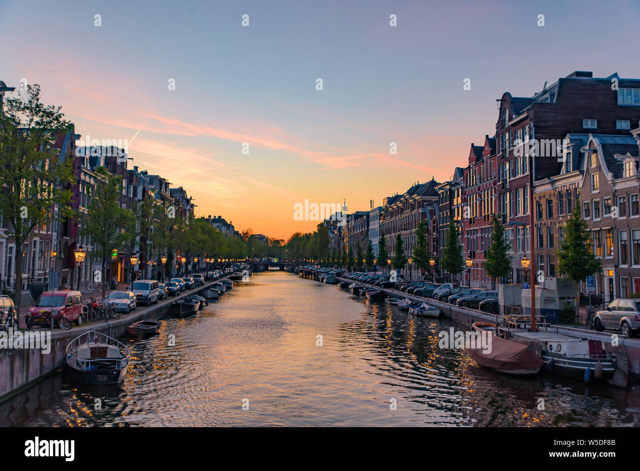 Gebäude, Bäume, und Boote auf dem Kanal bei Sonnenuntergang Zeit in Amsterdam, Niederlande Stockfoto