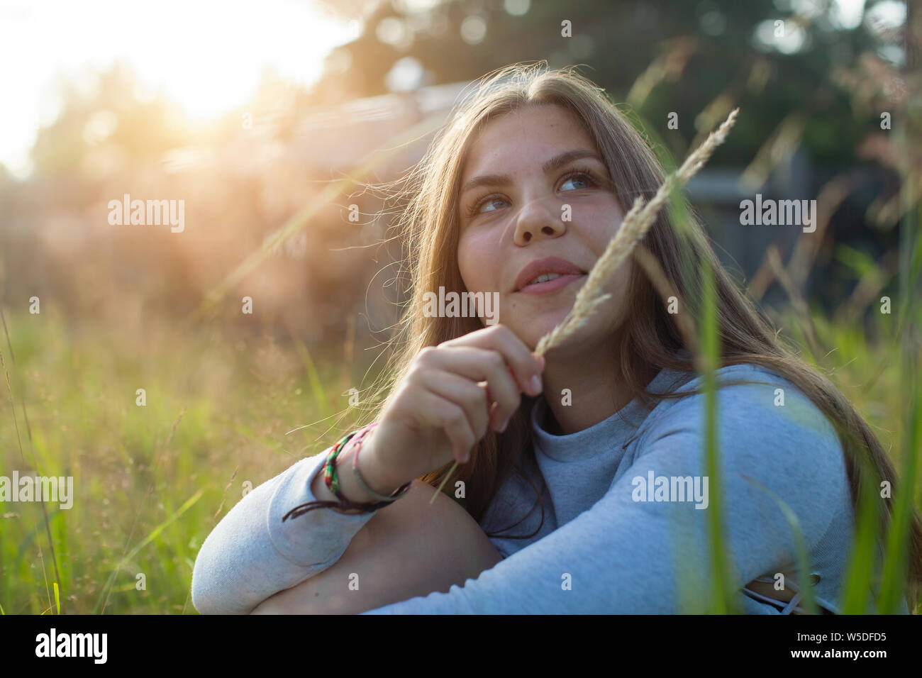 Teenage Mädchen im Gras sitzen im Sommer Landschaft bei Sonnenlicht. Stockfoto