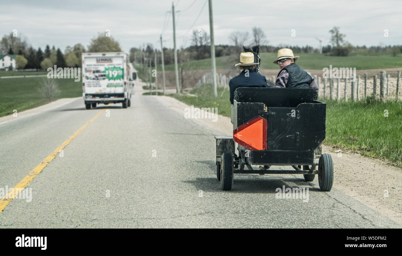 Zwei Mennoniten Jungs fahren ein Pferd Buggy auf der Seite der Straße im südlichen Ontario. Ein Blick zurück auf mich zu und er trägt eine Sonnenbrille. Stockfoto