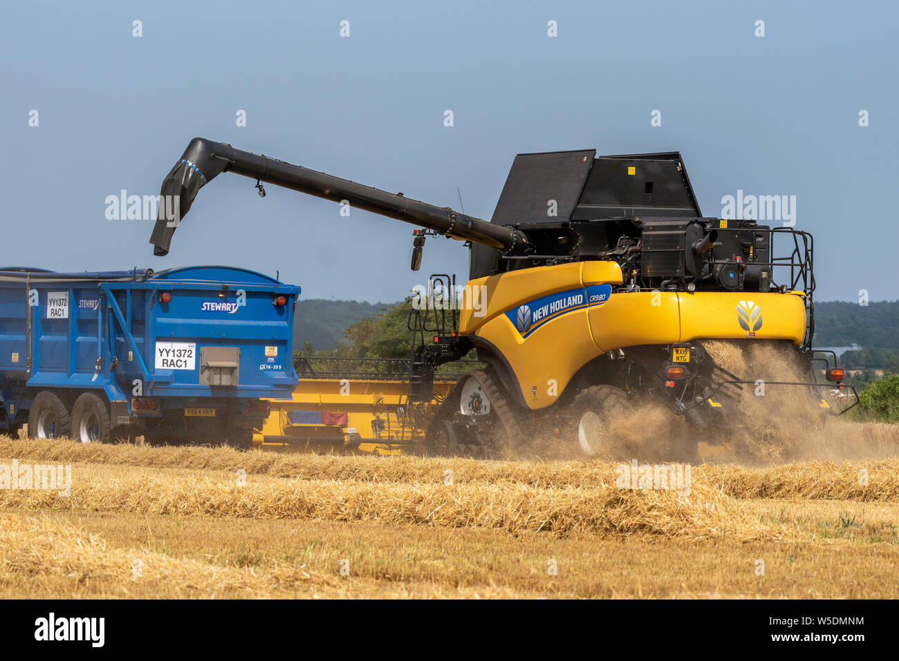 Cheltenham, Gloucestershire, England, UK. Mähdrescher offloading Gerste in einen Traktor Anhänger geerntet über eine Entleerrohr. Die Stockfoto