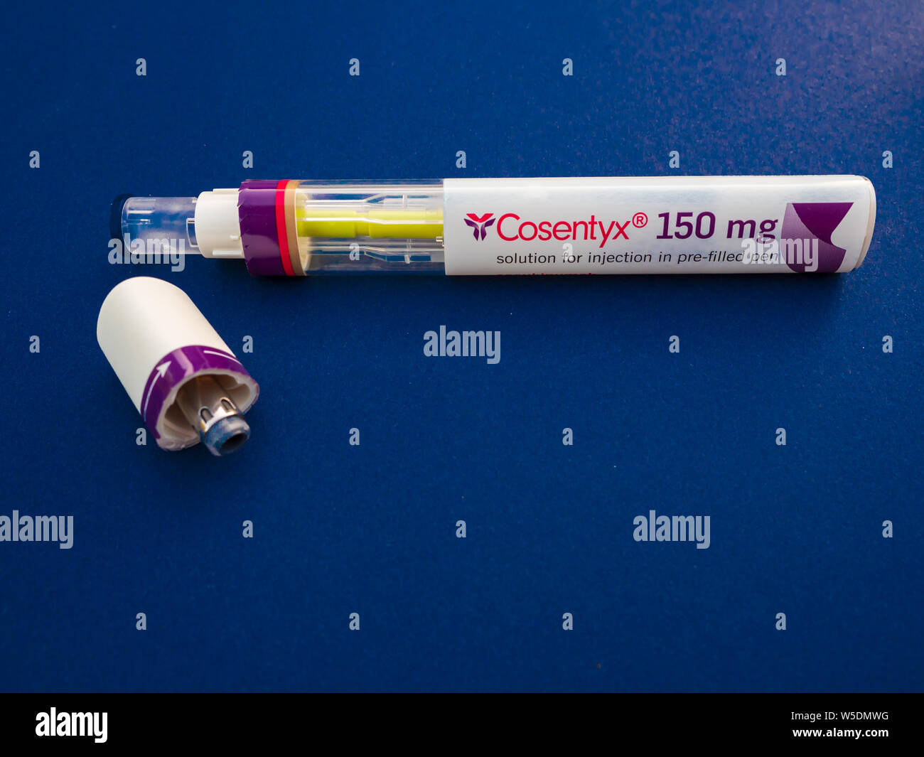 Eine gebrauchte Cosentyx (secukinumab) 150 mg Autom. Injektion, Pen, der die mit der gelben Markierung und der Deckel an der Seite auf einem blauen Hintergrund Stockfoto