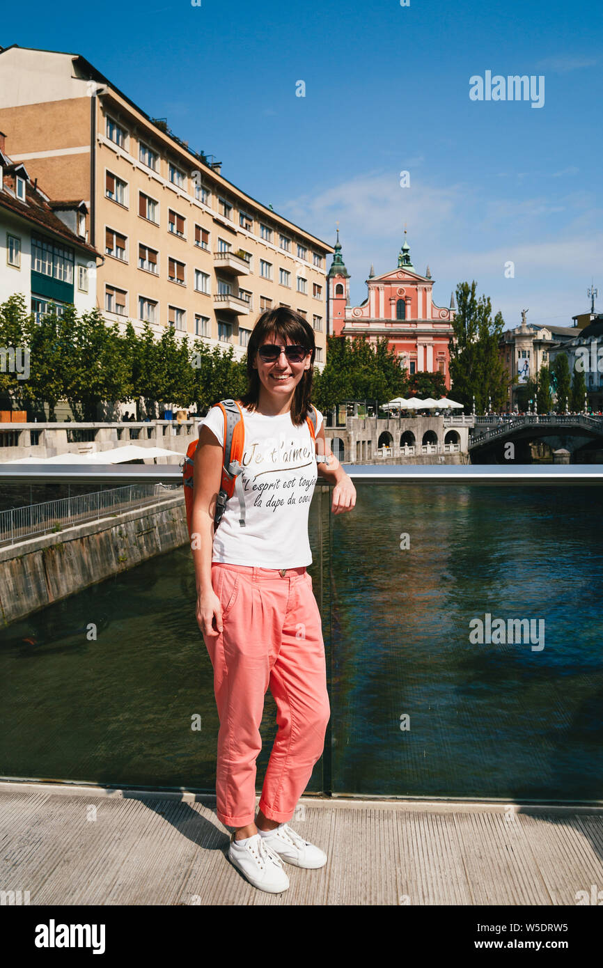 Junge lächelnde Frau Tourist auf einer Brücke in der Altstadt von  Ljubljana, Slowenien stehen, tragen weiße Hemd, weiße Turnschuhe und  Koralle Hose. Wit Stockfotografie - Alamy