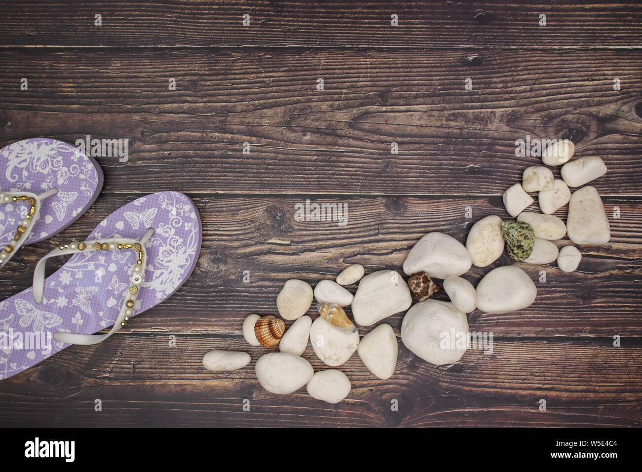 Weiße Steine und Muscheln mit lila Hausschuhe auf hölzernen Hintergrund Stockfoto