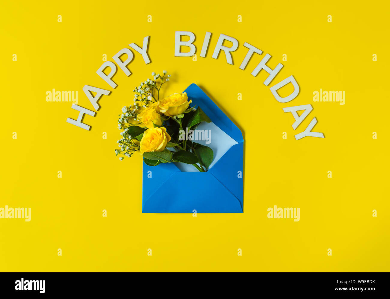 Gelbe Rosen und weißen Gypsophila in blauen Umschlag close-up auf gelben Hintergrund. Text alles Gute zum Geburtstag. Ansicht von oben, flach. Vorlage für Geburtstag Grüße Stockfoto