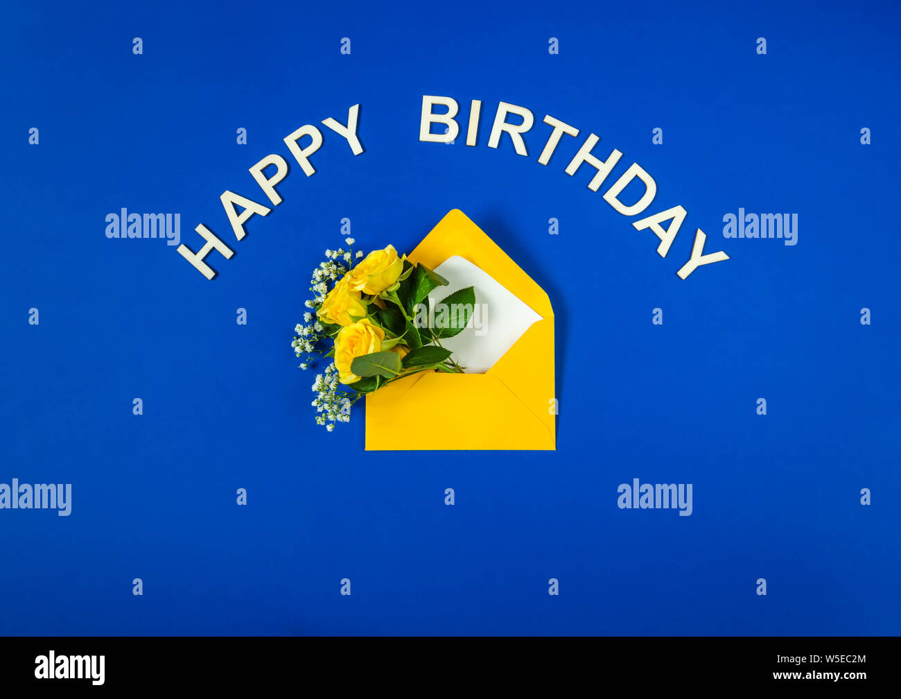 Gelbe Rosen und weißen Gypsophila im Umschlag close-up auf blauem Hintergrund. Text Happy Birthday, Holz- briefe. Ansicht von oben, flach. Für Geburt Vorlage Stockfoto
