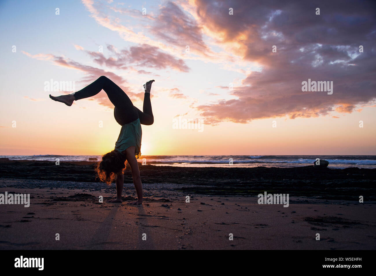 Sonnenuntergang Yoga am Strand mit glücklichen Frau Yogi eine wilde temperamentvoll Handstand. Stockfoto
