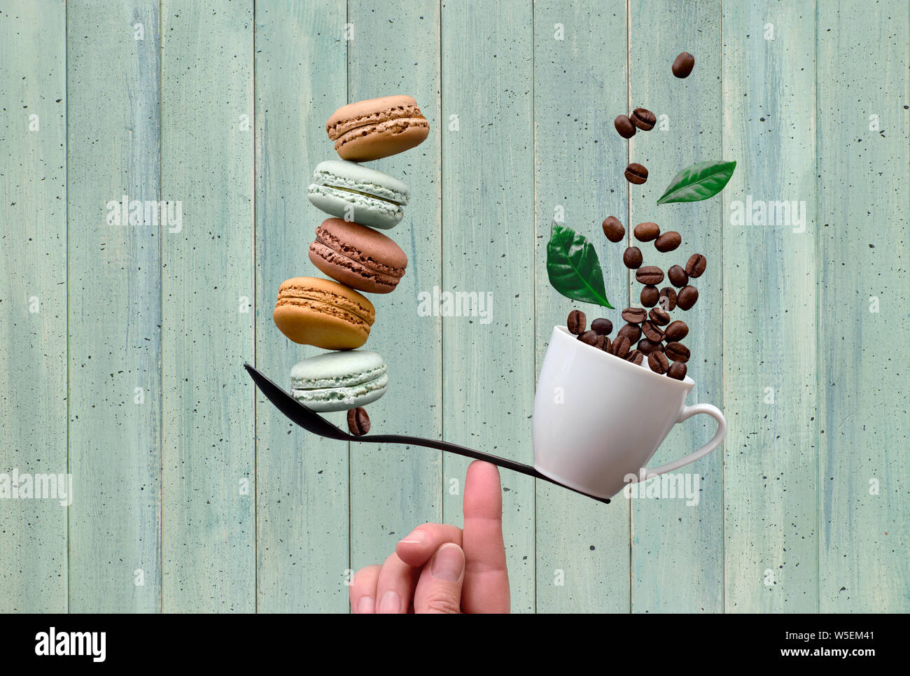 Gleichgewicht Konzept flach auf Minze farbige Holz- Hintergrund legen. Balancing Tasse Kaffee und macarons auf einem Finger Stockfoto