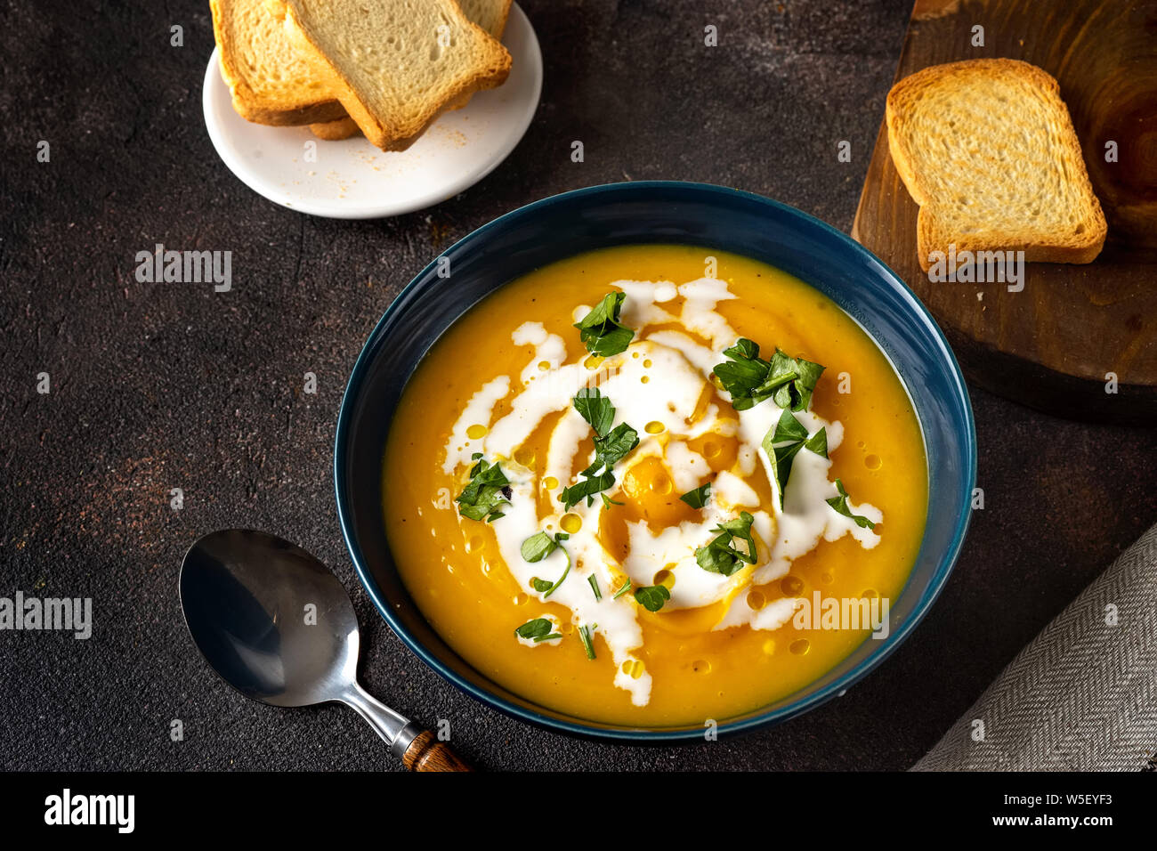 Kürbissuppe mit Sahne und Petersilie auf dunklen rustikalen Hintergrund Stockfoto Kürbissuppe mit Sahne und Petersilie auf dunklen rustikalen Hintergrund Stockfoto