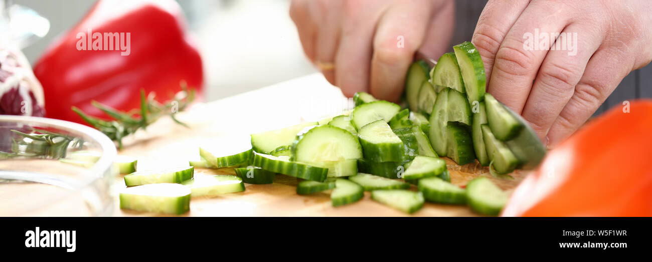Männliche Hände frische Gurke kleine Stücke hacken Stockfoto