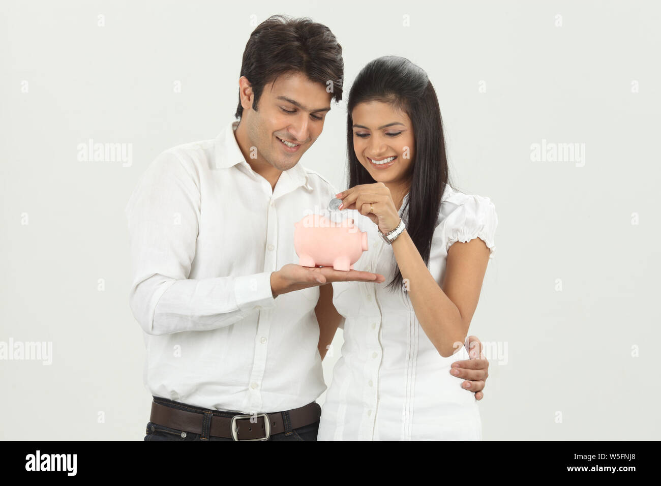 Frau, eine Münze in ein Sparschwein mit ihrem Ehemann Stockfoto