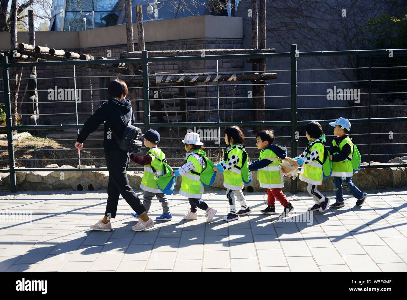 Kinder gekleidet in grün Kostüme, unter der Leitung eines Lehrers, in der Linie der Panda Halle gehen die Riesenpandas in Peking, China, 14. Stockfoto