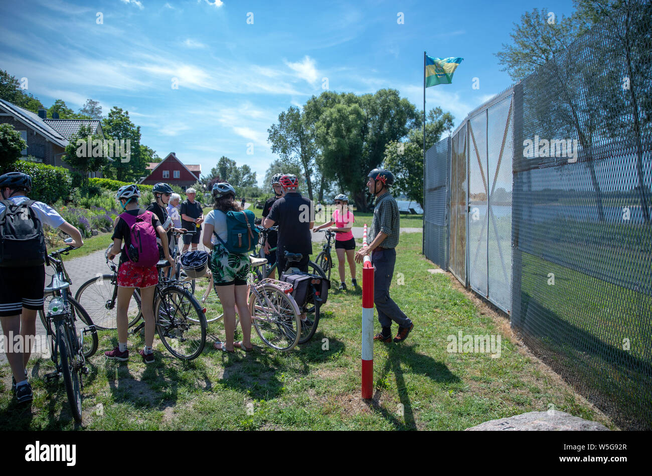 18. Juni 2019, Mecklenburg-Vorpommern, Rüterberg: Andreas Wagner, Mitarbeiter der Politische Memoriale e.V. und Leiter des Grenzhuus, erklärt die 30 Radfahrer auf Ihrer einwöchigen Tour entlang der ehemaligen innerdeutschen Grenze ein erhaltenes Stück Grenzzaun im Dorf Republik Rüterberg. Aufgrund seiner exponierten Lage in der DDR direkt an der westlichen Grenze, Rüterberg wurde komplett von einem drei Meter hohen Zaun umgeben. Einen Tag vor dem Fall der Berliner Mauer am 8. November 1989, die Bewohner in einer Sitzung gefordert, die "Öffnung der Grenzen der DDR" und erklärten ihre Stockfoto